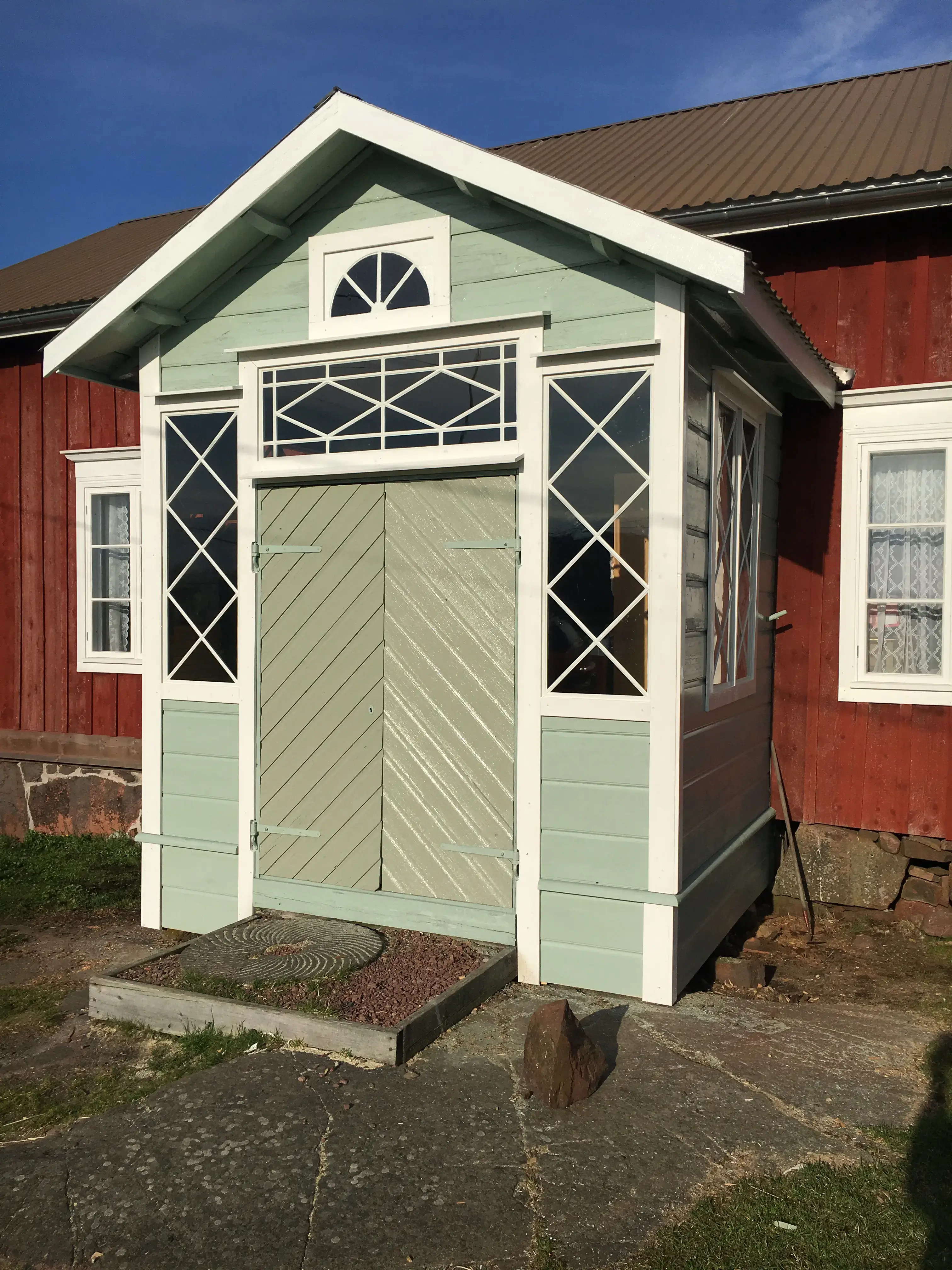 Exteriört fotografi som visar Jonesas lillstugas veranda; en utstickande farstubyggnad målad i mintgrönt mot en i övrigt faluröd träbyggnad i ett plan.