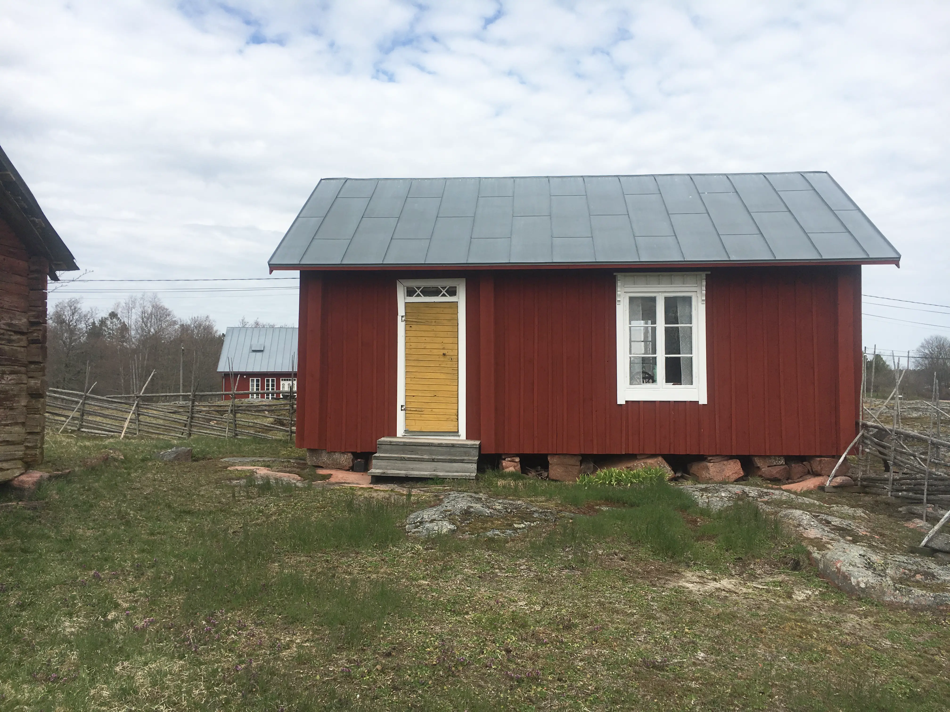 Fotografi av Sjöbloms emigrant- och torparmuseum, exteriör, en halvmulen dag. Bilden visar en bred, låg, falurödfärgad äldre träbyggnad. Just bakom syns en gammal gärdsgård. Marken omkring är mossig och stenig.